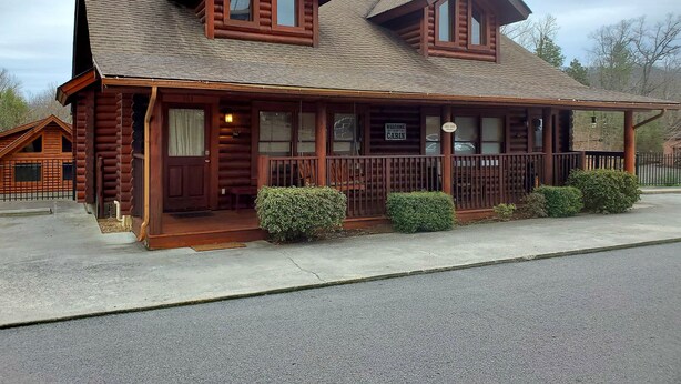 A log cabin with a porch, two windows, and a sign welcoming guests to the cabin.