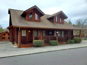A log cabin with a porch, two windows, and a sign welcoming guests to the cabin.