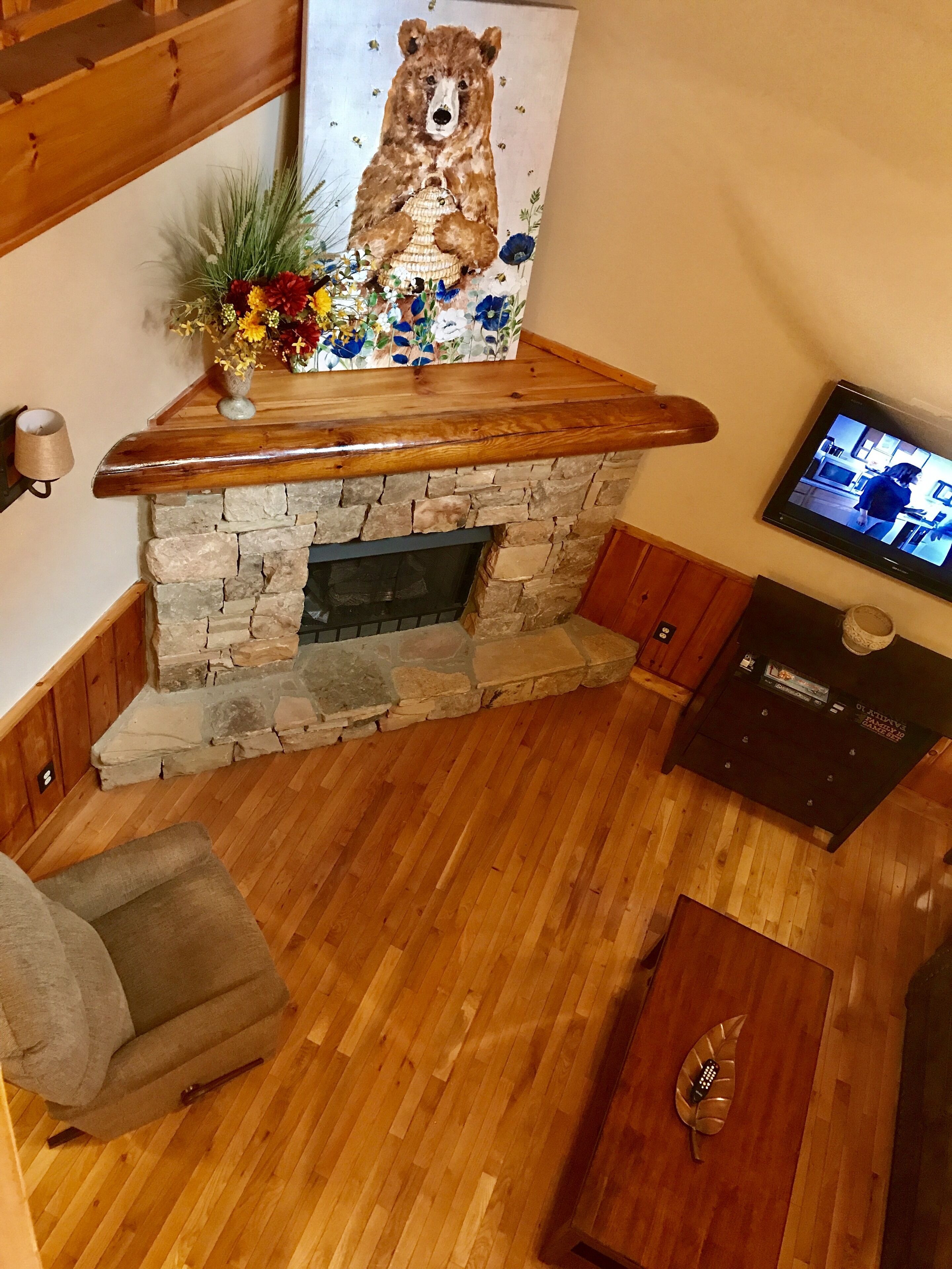 Ein gemütliches Wohnzimmer mit Kamin aus Stein, einem Bärenbild und einem Fernseher.