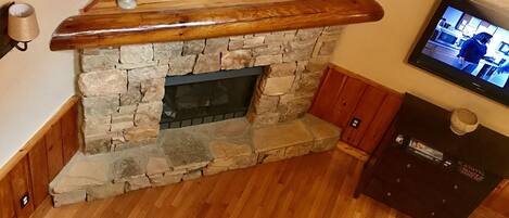 A cozy living room with a stone fireplace, a bear painting, and a television.