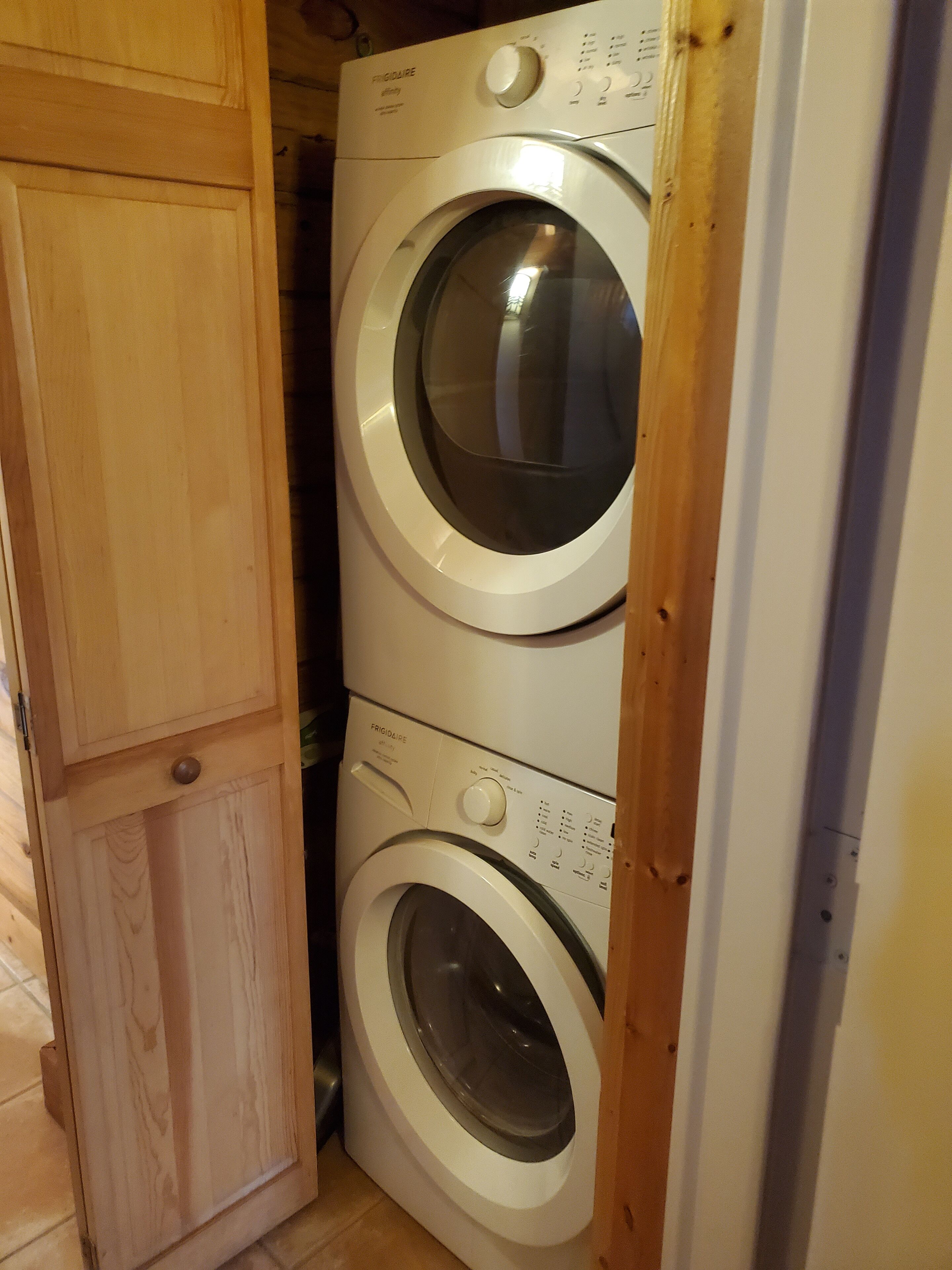 Une machine à laver et un sèche-linge superposés dans une buanderie équipée d’armoires en bois.