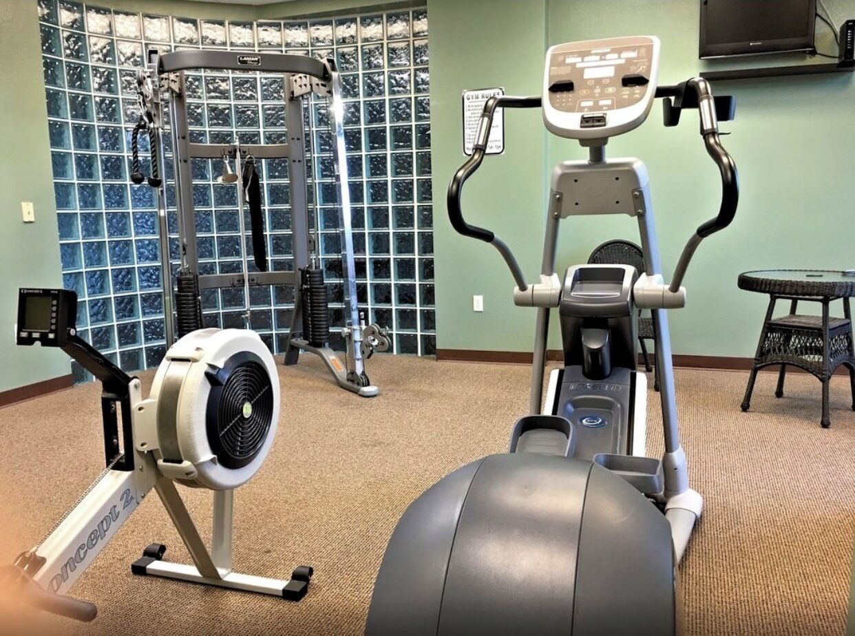 A gym with cardio machines, weightlifting equipment, and a wall-mounted TV.