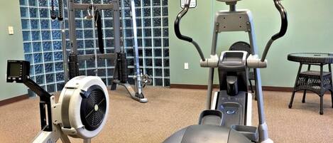 A gym with cardio machines, weightlifting equipment, and a wall-mounted TV.