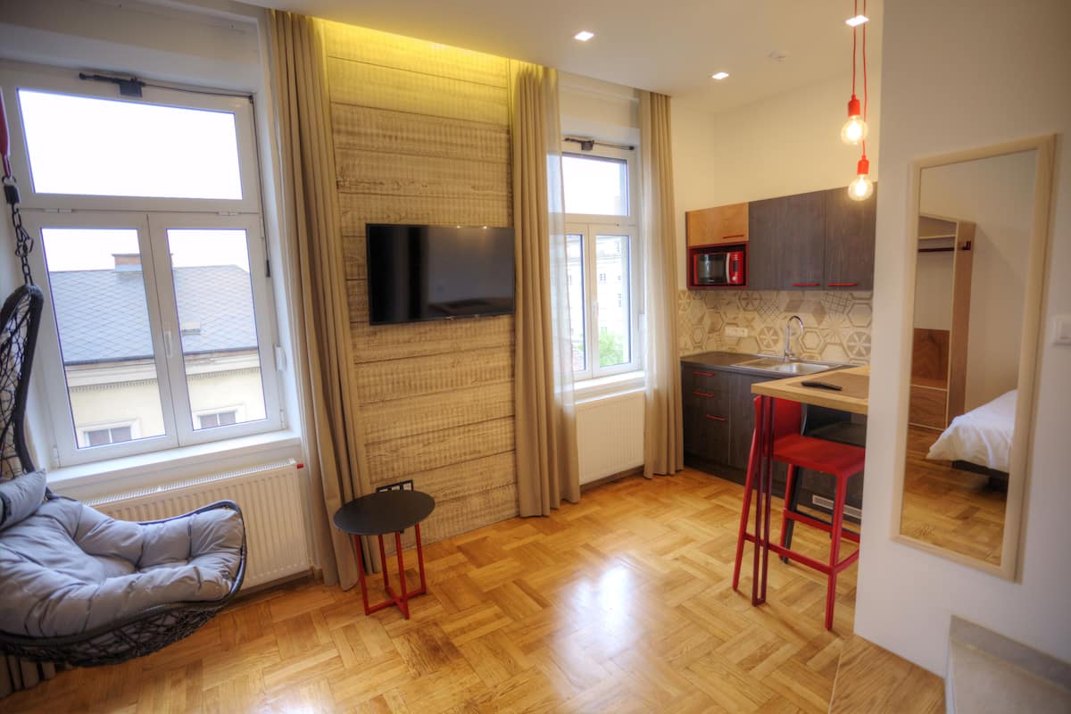 Ein gemütlicher Wohnbereich mit Sofa, kleinem Tisch, Küchenzeile mit Spüle und an der Wand montiertem Fernseher.