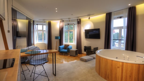 Ett modernt vardagsrum med ett matbord i trä, blå stolar, en blå soffa, ett stort fönster, en tv och ett badkar i trä.