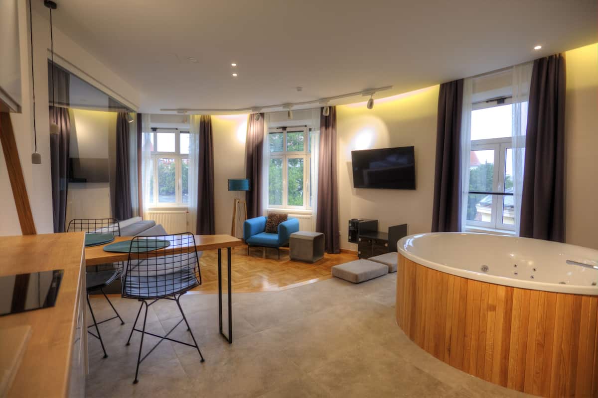 Ein modernes Wohnzimmer mit einem Holzespeisetisch, blauen Stühlen, einem blauen Sofa, einem großen Fenster, einem Fernseher und einer Holzbade-Wanne.