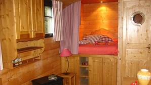 Ein gemütliches Cabin-Zimmer mit Bett, kleinem Tisch, Holzschrank, Herd und einer Tür mit Fenster.