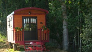 Eine kleine Holzhütte mit Veranda und roten Stühlen, umgeben von Bäumen.