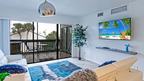 A modern living room with a large sliding glass door leading to a balcony, a flat-screen TV mounted on the wall, and a cozy seating area with a patterned rug.