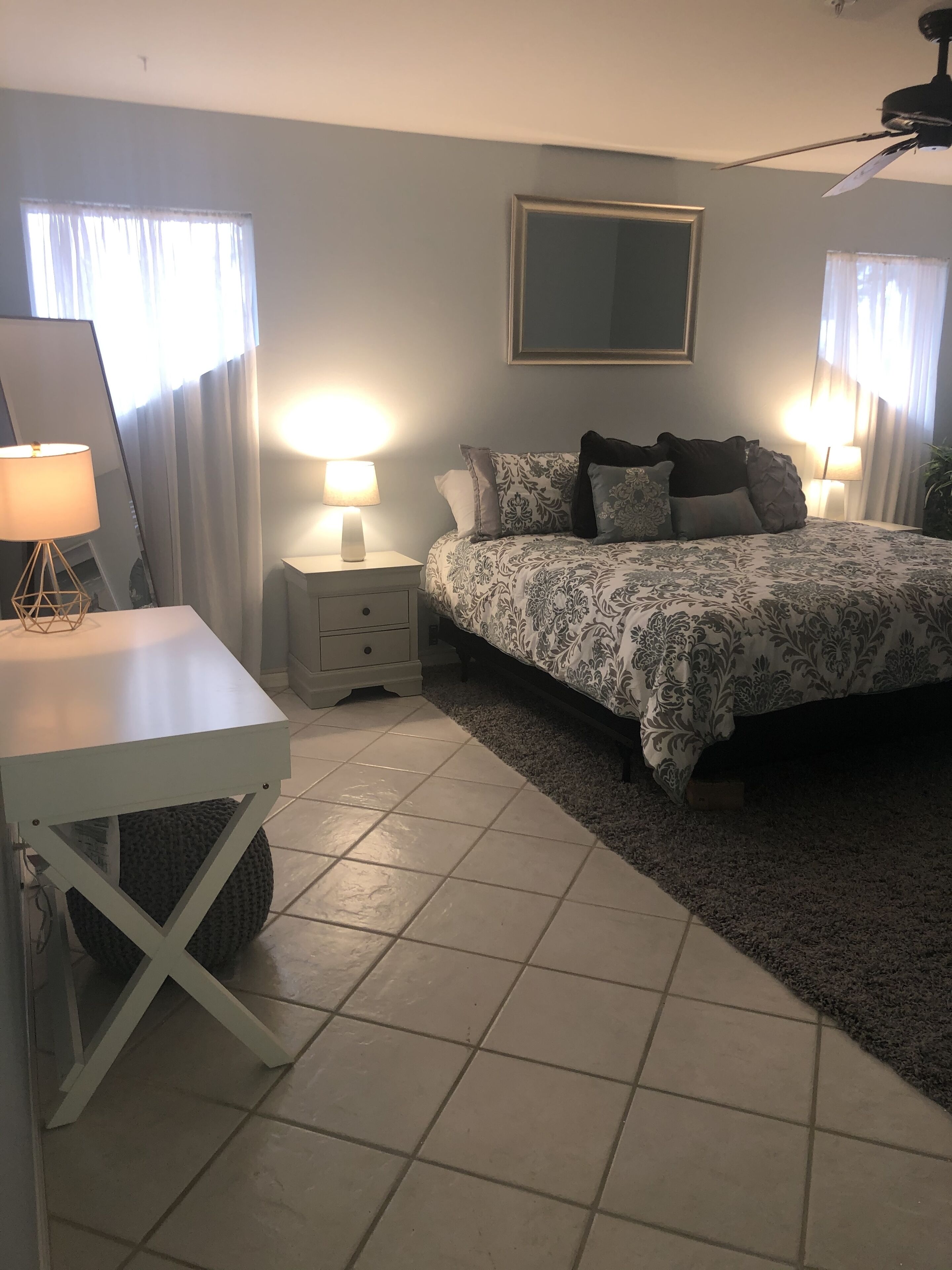 A bedroom with a bed, two bedside tables, a mirror, and a ceiling fan.