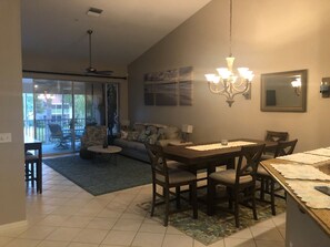 A dining area with a table and chairs, a chandelier, and a view through a glass door to an outdoor balcony.
