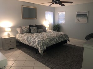 A bedroom with a bed, nightstands, a ceiling fan, a large mirror, and a window with blinds.