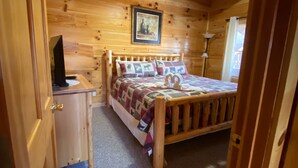 A wooden cabin bedroom with a bed, a nightstand, a framed picture on the wall, and a ceiling light. - Beautiful 2 bedroom 2 bath clean log cabin.  (Sevierville)
