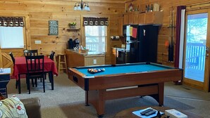 A cozy wooden cabin interior with a pool table, a dining area, and a living room with a sofa and coffee table. - Beautiful 2 bedroom 2 bath clean log cabin.  (Sevierville)