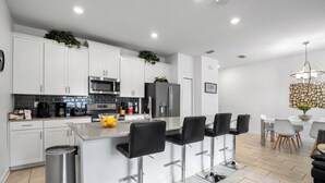A modern kitchen with white cabinets, stainless steel appliances, and a bar area with black stools. - Resort Style, close to Disney and other parks Wlking Distance to Oasis Club (Davenport)