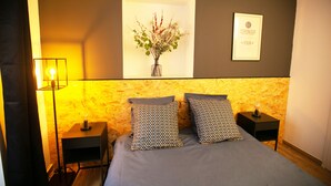 Une chambre à coucher avec un lit, deux tables de chevet, une lampe fixée au mur, un tableau représentant des fleurs et une citation inspirante sur le mur.