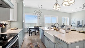 A modern kitchen with a large island, a dining area with a view, and a spacious living area with a balcony. - "Soul Surfer" Dream Vacation Home w/ Direct Beach Access on the East End of Panama City Beach. Private Pool, Game Room, Large Suites + More! (Panama City Beach)