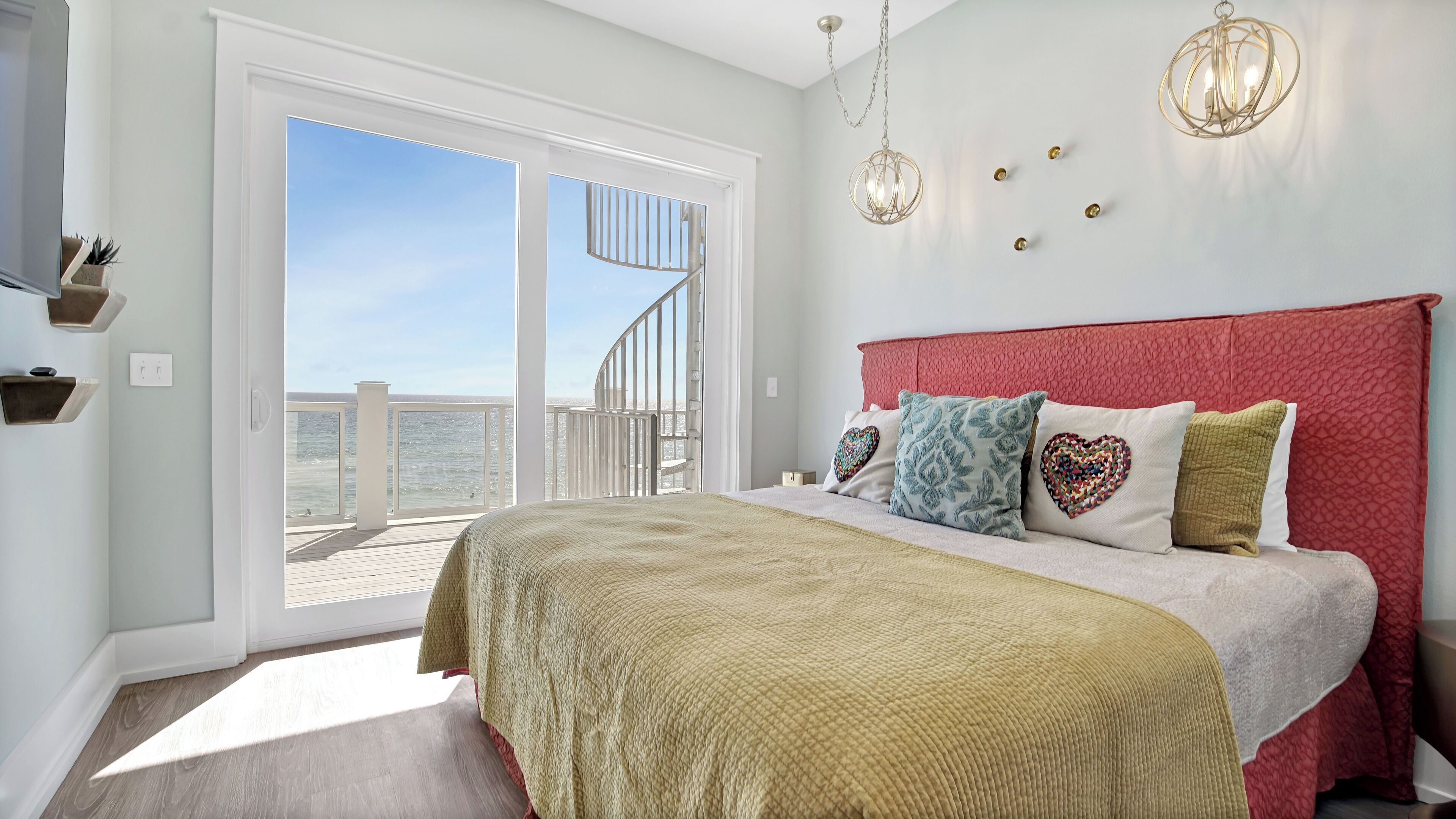 A bedroom with a large bed, a red headboard, and a view of the ocean through a sliding door.
