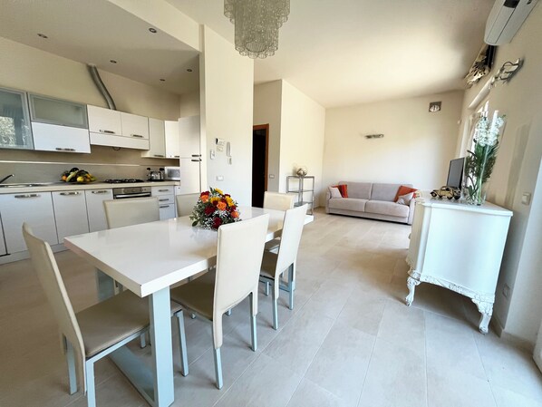 A modern kitchen with white cabinets, a dining table with chairs, and a living area with a sofa and a small white cabinet.