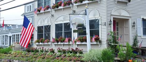 A building with a 'VACANCY' sign, American flags, and flower boxes on the windows.