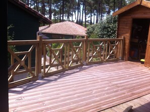 A wooden deck with a railing, a small building with a tiled roof, and a forested background.
