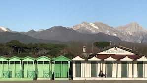 Una fila di edifici verdi e bianchi con montagne sullo sfondo, con la scritta 'SACRO CUORE'.