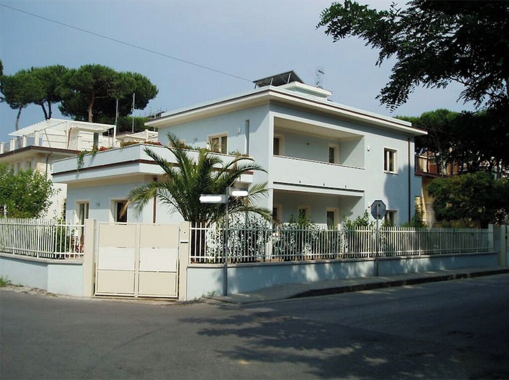 A two-story residential building with a flat roof, a gated entrance, and a small balcony on the upper floor.