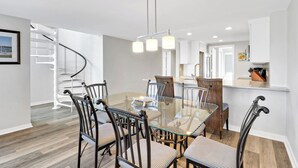 A modern dining area with a glass table, striped chairs, and a spiral staircase.