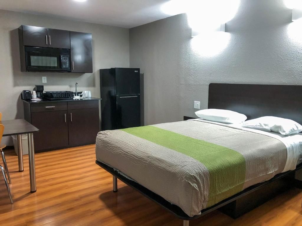 Quarto de hotel com cama, escrivaninha, micro-ondas e geladeira.