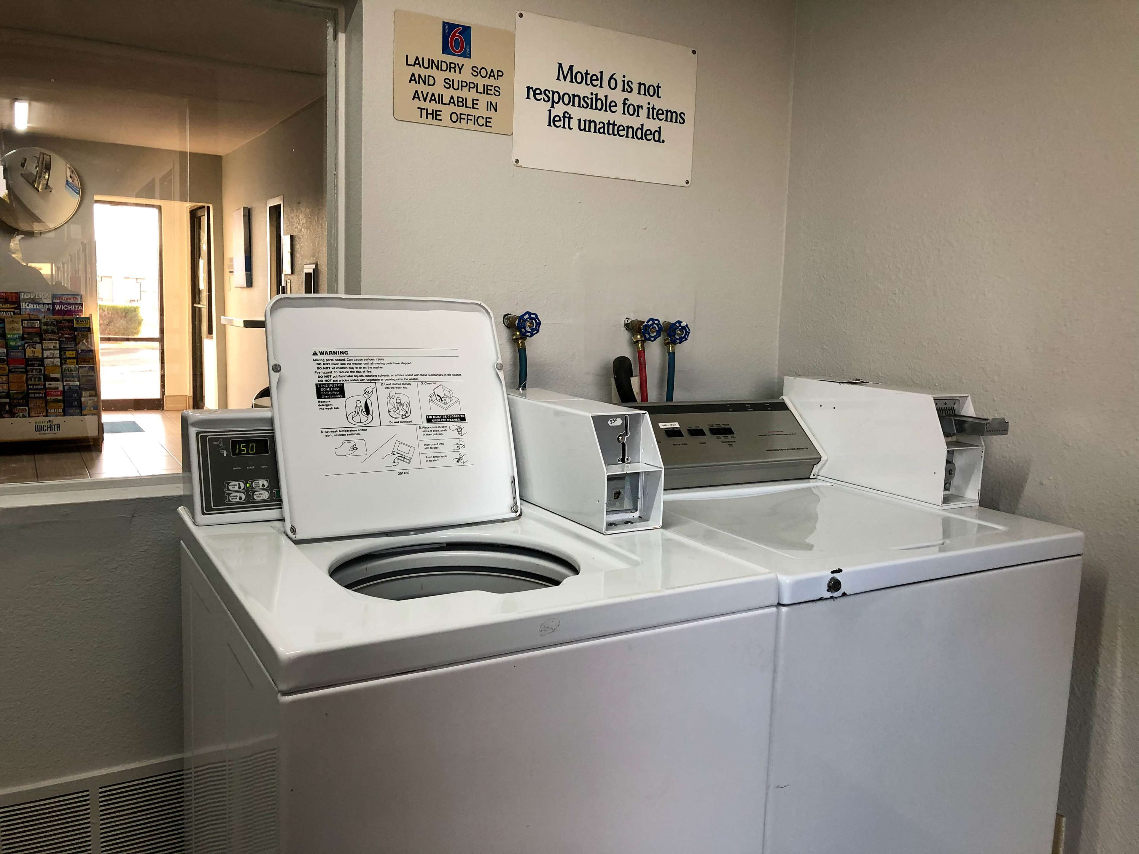 Un cuarto de lavandería con lavadora y secadora, carteles que indican la disponibilidad de productos de limpieza, y un letrero con instrucciones de seguridad.