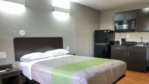 A hotel room with a bed, a nightstand, a kitchenette with a microwave, and a refrigerator. - Studio 6 Wichita, KS - Airport (Wichita)