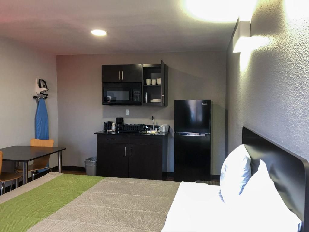 A hotel room with a bed, a small kitchenette, a microwave, and a refrigerator.