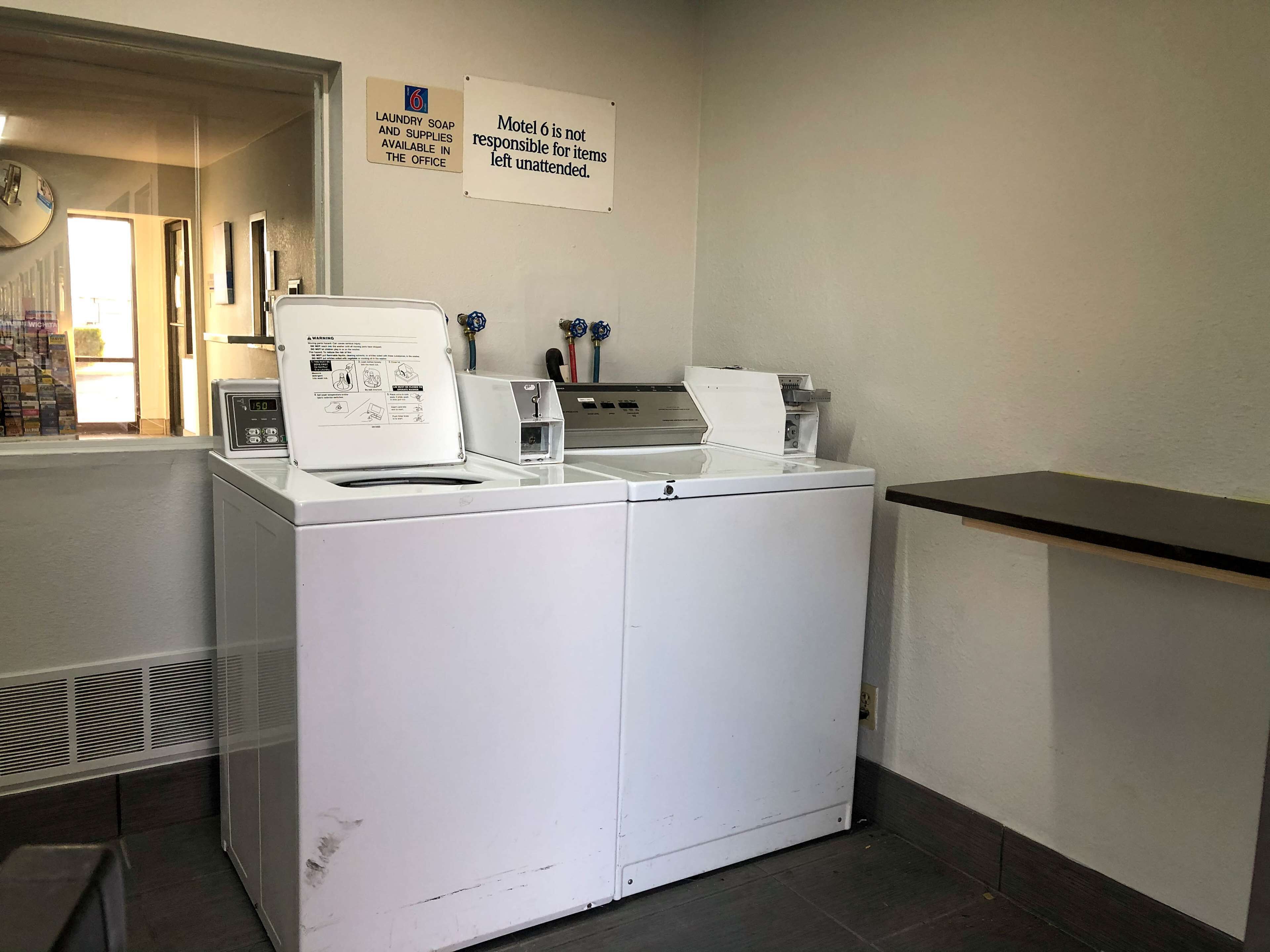 Een wasruimte met een wasmachine en droger, een magnetron, en een bordje waarop staat dat wasmiddel verkrijgbaar is bij de receptie.