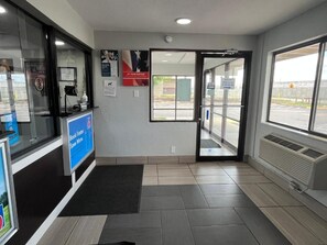 Zona de recepción con puerta de vidrio que da al exterior, mostrador de recepción y cartel que indica acceso nocturno.