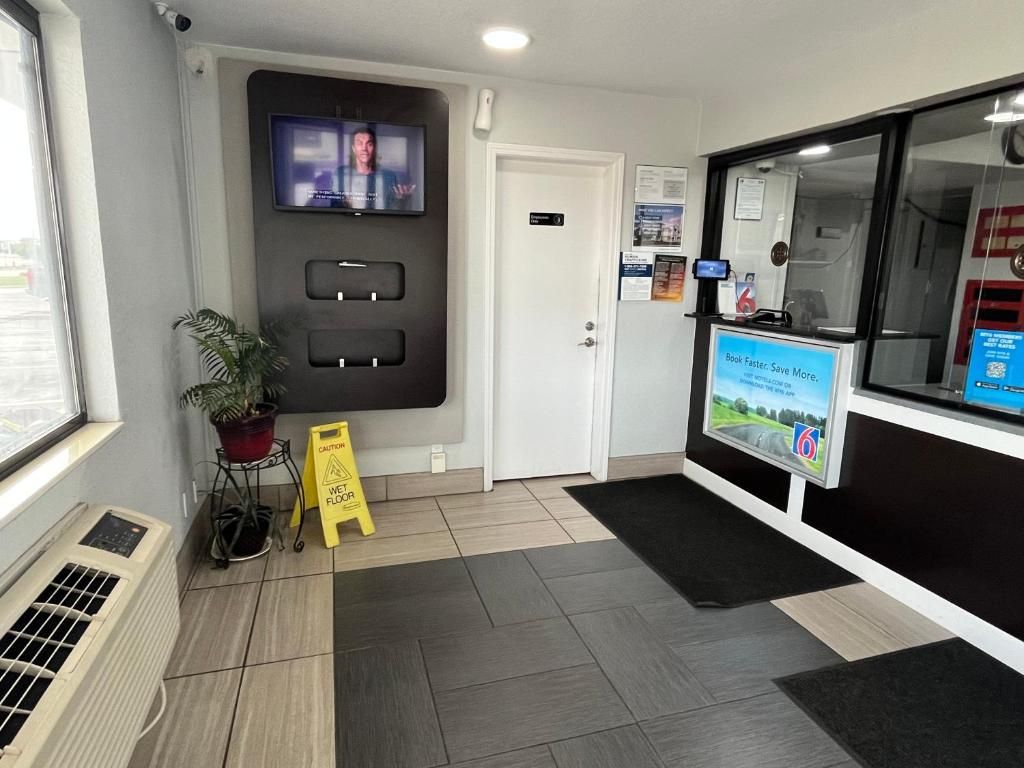 A reception area with a television, a door, a wet floor sign, and a digital display.