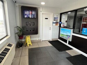 Zona de recepción con televisor, una puerta, señal de piso mojado y pantalla digital.