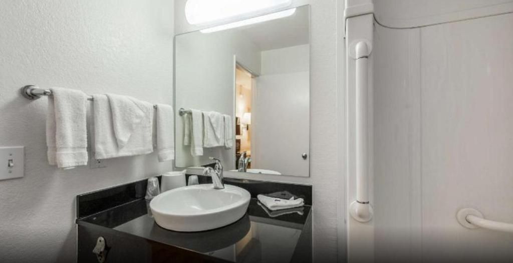 Un baño con lavamanos blanco, espejo y barra para toallas.