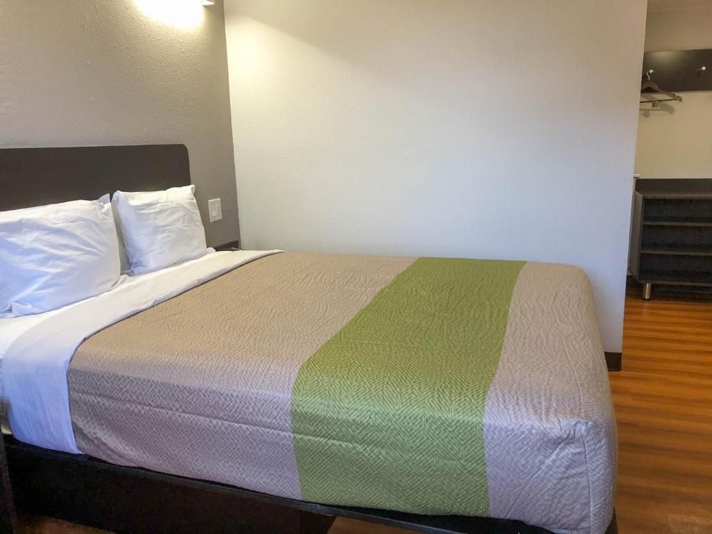 A single bed with a headboard, a green and white bedspread, and a wooden floor.