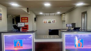 A reception area with two desks, each with a 'studio 6 extended stay' sign, a clock, and framed pictures on the wall. - Studio 6 Wichita, KS - Airport (Wichita)