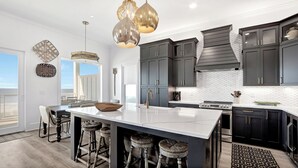 A modern kitchen with dark cabinets, a large island with stools, pendant lighting, and a view to the outside.
