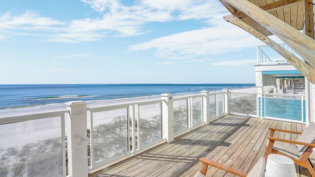 A wooden deck with a view of the ocean, a pool area, and a covered seating area.