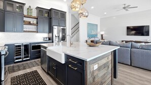 A modern kitchen with dark cabinets, a white island, and a dining area with a gray sofa.