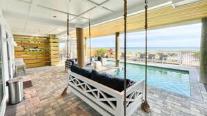 A poolside area with a swing chair, a small pool, and a view of the ocean.