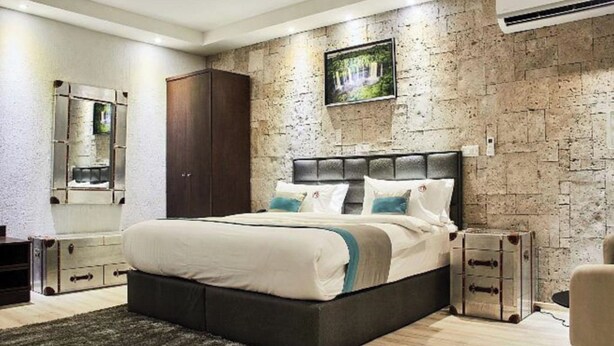 Un dormitorio moderno con una cama grande, una pared de piedra y un televisor montado.