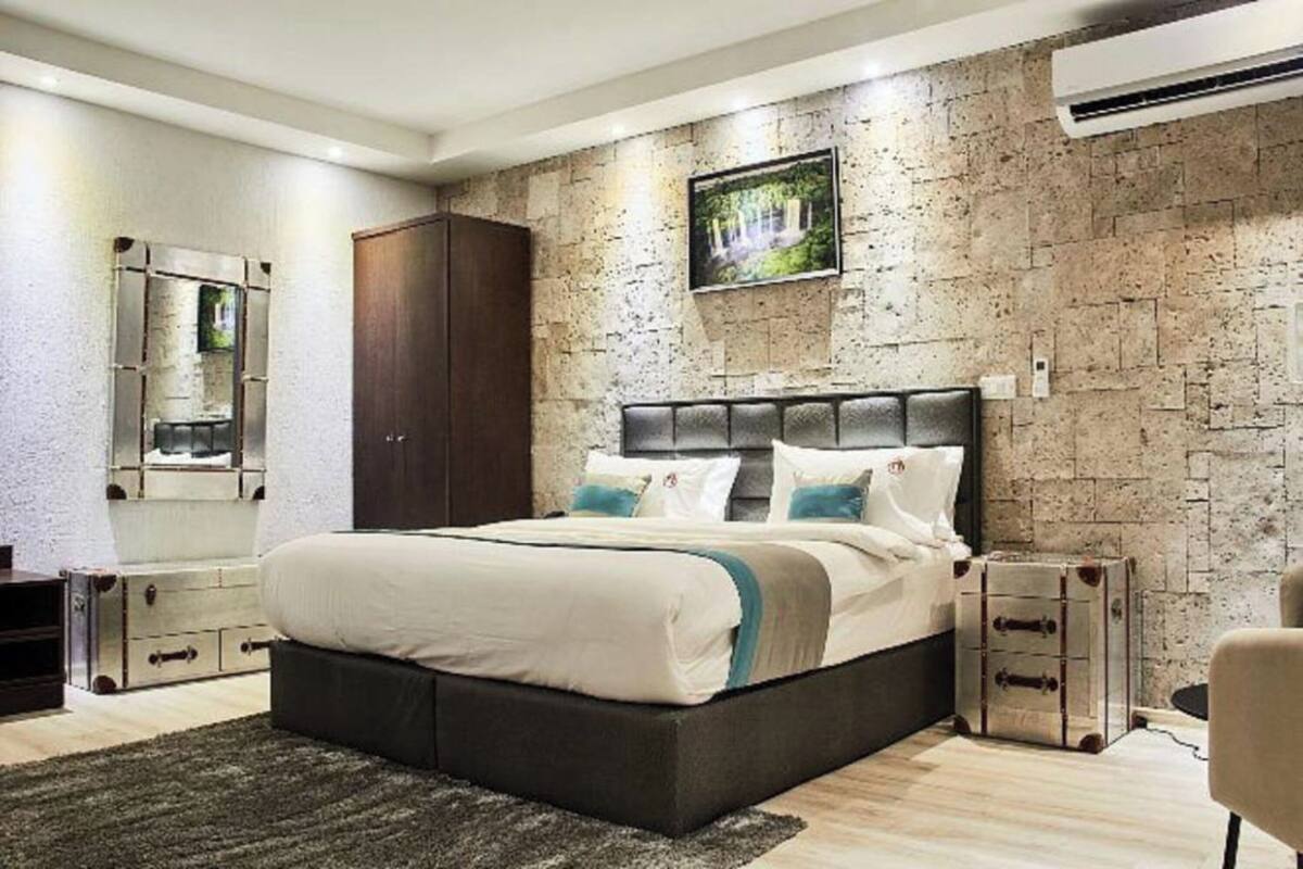 A modern bedroom with a large bed, a stone wall, and a mounted TV.