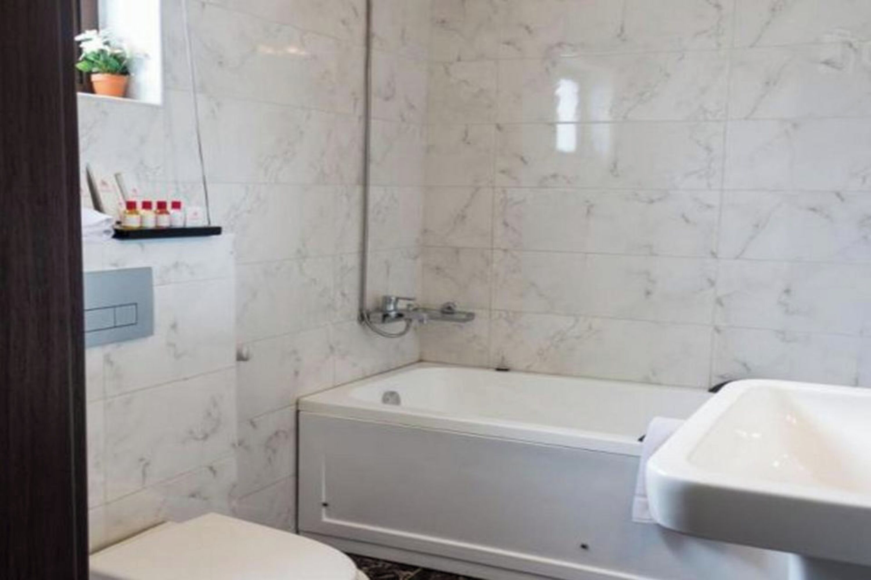 Une salle de bain avec une baignoire, des toilettes et un lavabo. On y trouve une étagère avec des articles de toilette et une plante en pot.