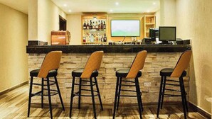Zona de bar con pared de piedra, taburetes, una pantalla de televisión y una estantería con botellas.