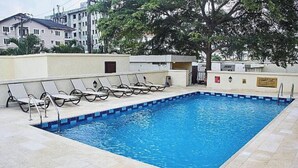 Una piscina rectangular con borde de azulejos, rodeada de sillones de descanso y una solana también de azulejos.