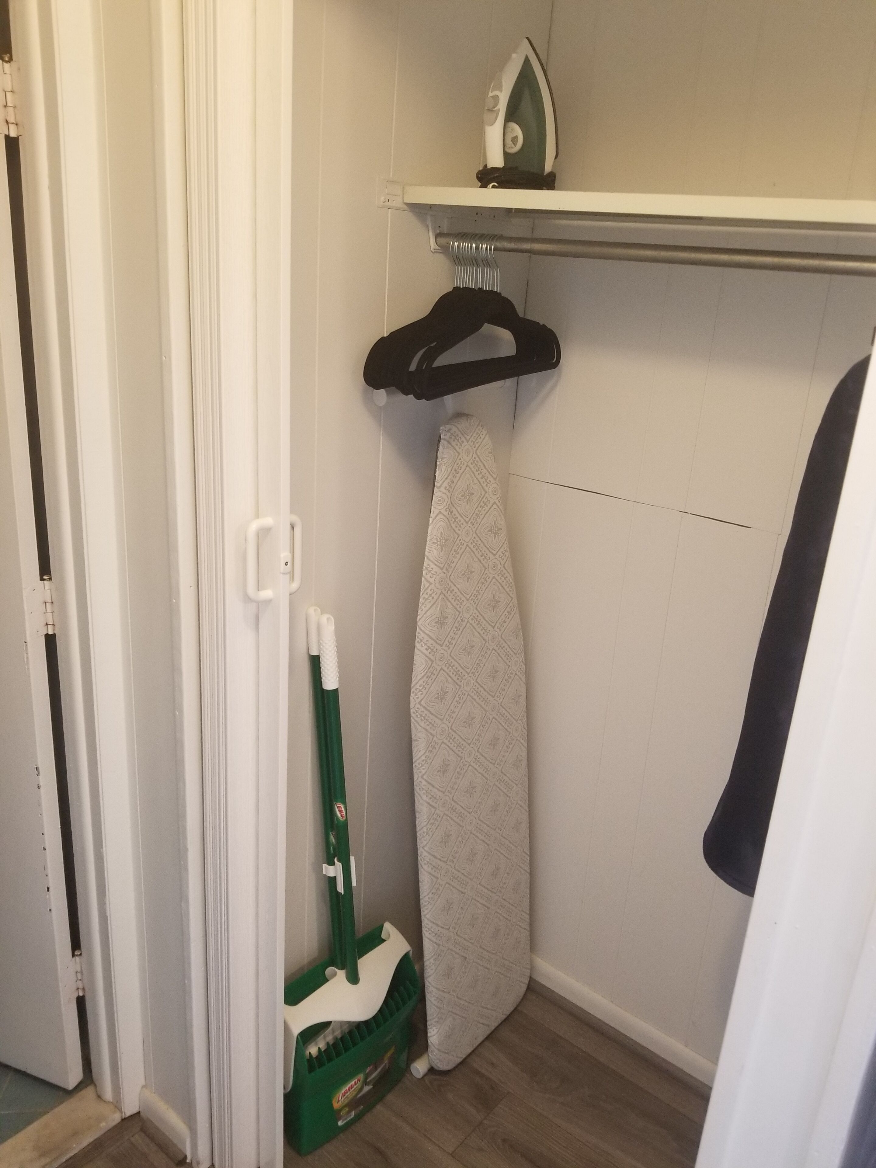 A small laundry area with an iron, ironing board, and cleaning supplies.