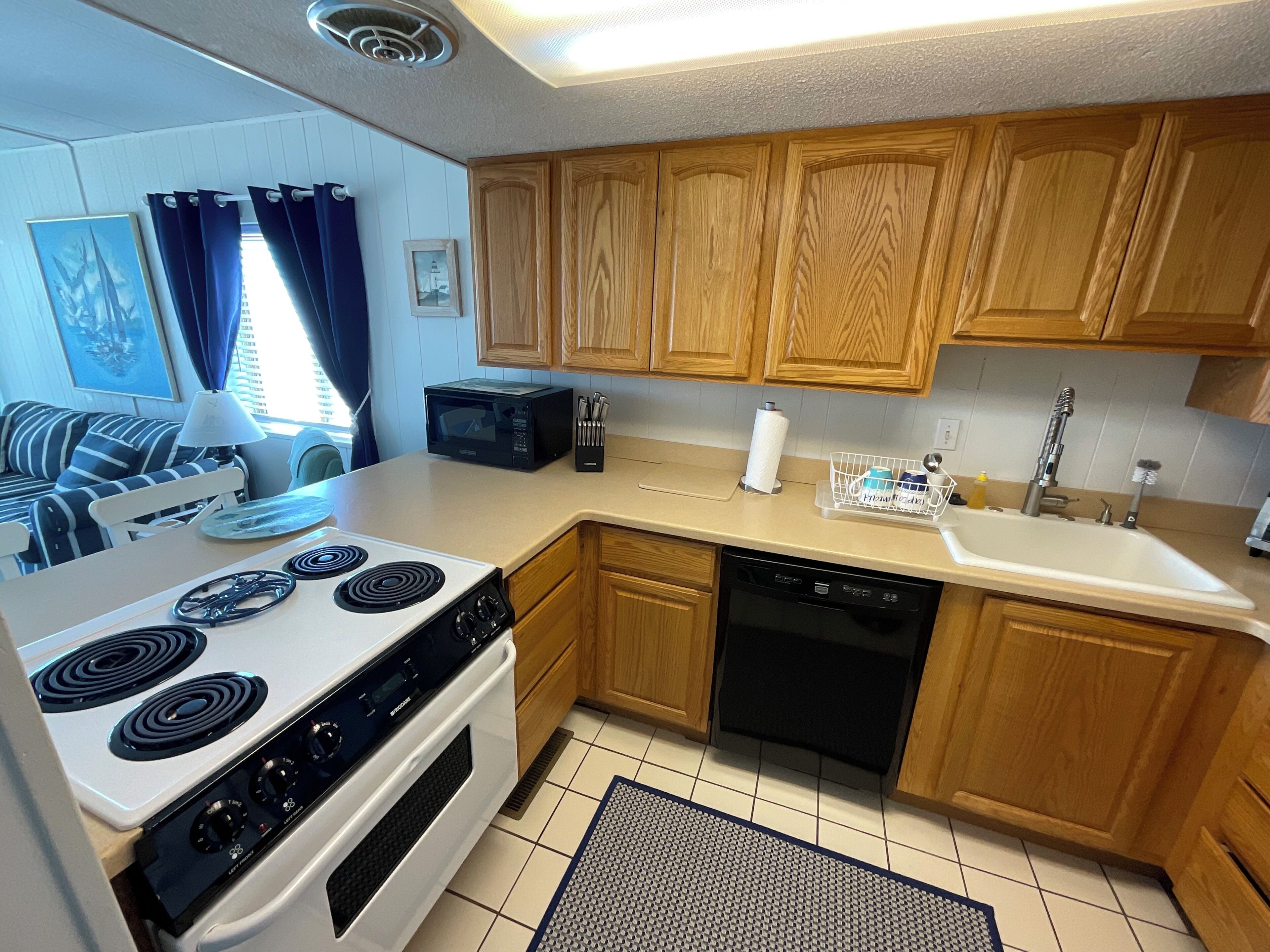 A compact kitchen with wooden cabinets, a microwave, a stove, and a dishwasher.